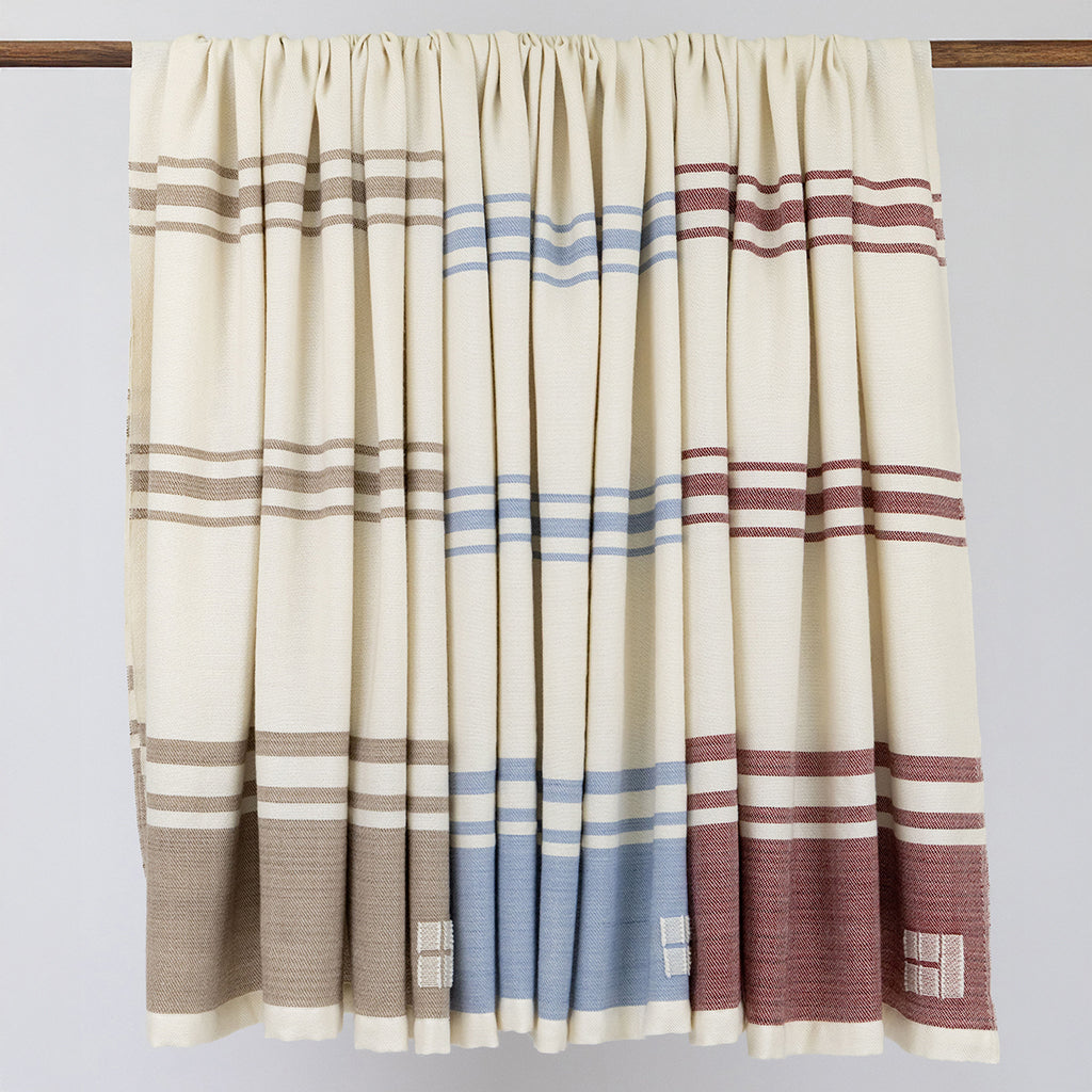Striped curtain with brown, blue, and red patterns on a wooden rod against a light gray background.